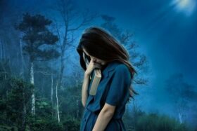 Ein Mädchen steht traurig mit einer Bibel in der Hand vor einer dunklen Landschaft mit Bäumen